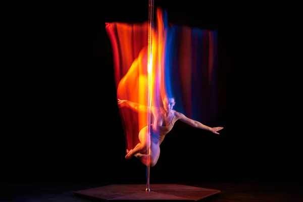 Flight. Young girl performing pole dance isolated over black studio background with mixed neon lights. Concept of sport and dance, beauty of movements, action, modern style