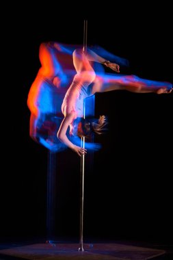 Sanatsal yaşam tarzı. Siyah stüdyo arka planında karışık neon ışıklarıyla striptiz dansı yapan genç bir kız. Spor ve dans kavramı, hareketlerin güzelliği, eylem, modern tarz.