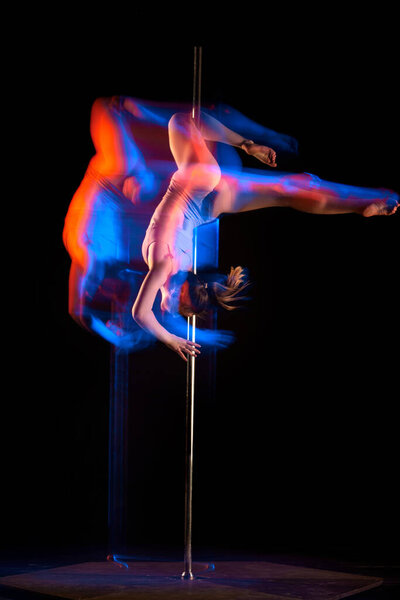 Artistic lifestyle. Young girl in bodysuit performing pole dance isolated over black studio background with mixed neon lights. Concept of sport and dance, beauty of movements, action, modern style