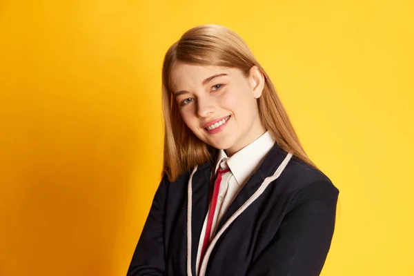 Excellent student, Portrait of beautiful young girl in uniform smiling, posing over yellow studio background. Concept of youth, beauty, fashion, lifestyle, emotions, facial expression. Ad