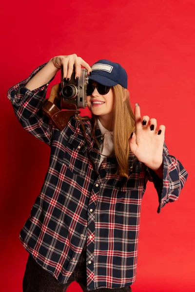 照片中的瞬间 身穿格子衬衫 帽子和太阳镜的年轻貌美女子 在红色摄影棚的背景下摆出照相相机的姿势 美的概念 生活方式 面部表情 — 图库照片