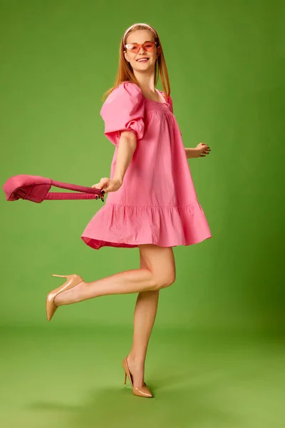 积极的情绪 美丽的金发碧眼的小女孩穿着可爱的粉色衣服 脚跟在绿色的工作室背景之上 生活方式 面部表情的概念 — 图库照片