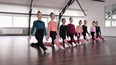 Group of little girls, children, gymnasts sitting on twine in a line. Indoor training. Flexibility. Concept of sportive lifestyle, childhood, education, health, professional sport.