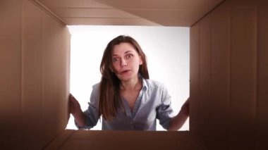 Karton kutuyu duygusal olarak açan genç bir kız, mutlu ve şaşırmış bir yüzle içine bakıyor. İnternetten alışveriş, satış ve nakliye. Alışveriş, dağıtım, duygu ve yüz ifadesi kavramı
