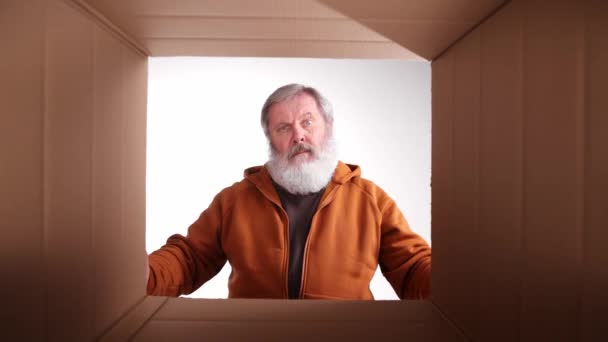 疑わしい顔 老人の荷解き 段ボール箱を開けると感情的に内部を見て 納入品の評価 買い物 感情や表情の概念 — ストック動画