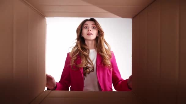 年轻姑娘穿着时髦的粉色夹克 打开包装 打开纸板箱 满脸不悦 货物质量差 情绪及面部表情的概念 — 图库视频影像