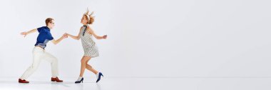 Aktif hobi. Gri stüdyo arka planında dans eden şık elbiseli genç adam ve kadın. Sanat anlayışı, eski tarz, hobi, parti, eğlence, hareketler, 60 'lar, 70' ler kültürü. Pankart