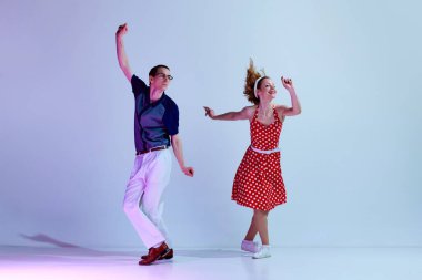 Genç pozitif bir çift, renkli kostümlü bir kadın ve erkek gradyan mavi mor stüdyo arka planına karşı retro dansı yapıyorlar. Sanat anlayışı, retro tarzı, hobi, parti, eğlence, 60 'lar, 70' ler kültürü