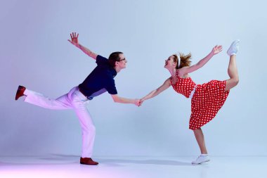 Güzel genç bir çift, renkli kostümlü bir erkek ve bir kız. Mor renkli stüdyo arka planına karşı retro danslar yapıyorlar. Sanat, retro tarzı, parti, eğlence, 60 'lar, 70' ler kültür konsepti