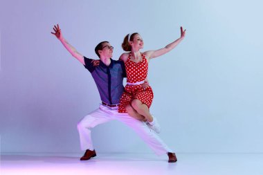 Güzel genç bir çift, renkli kostümlü bir erkek ve bir kız. Mor renkli stüdyo arka planına karşı retro danslar yapıyorlar. Sanat, retro tarzı, parti, eğlence, 60 'lar, 70' ler kültür konsepti