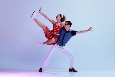 Güzel genç bir çift, renkli kostümlü bir erkek ve bir kız. Mor renkli stüdyo arka planına karşı retro danslar yapıyorlar. Sanat, retro tarzı, parti, eğlence, 60 'lar, 70' ler kültür konsepti
