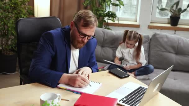 满头胡须的商人 父亲坐在桌旁 在家里的笔记本电脑上和他的小女孩坐在沙发上画画 家庭时间 自由职业 远程工作 情感的概念 — 图库视频影像