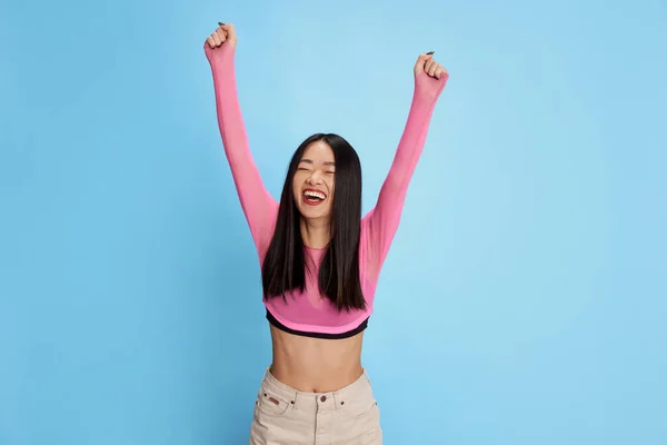 Winner. Feeling extremely happy. Portrait of happy excited young girl smiling, posing against blue studio background. Concept of emotions, facial expression, fashion, youth, lifestyle. Ad