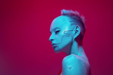 Pembe stüdyo arka planında parlak ışıkta çıplak omuzlu fütürist sayborg robot imajı çizen genç kız. Dijitalleştirme. Siber punk tarzı. Fütürizm kavramı, sürrealizm, dijital dünya, robot