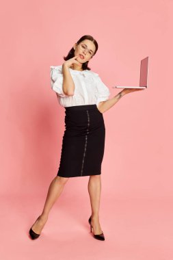 Pembe stüdyo arka planında dizüstü bilgisayarla poz veren resmi güzel iş kadınının tam boy portresi. İş anlayışı, eğitim, meslek, duygular, moda. Ad