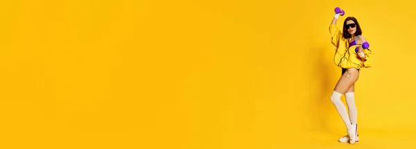 穿着时髦运动服的年轻貌美的黑发女子 摆着淡黄色背景的哑铃 运动的概念 健康的生活方式 班纳广告的复制空间 — 图库照片