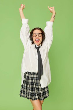 Mutlu ve pozitif. Kareli etekli, beyaz gömlekli, yeşil arka planda gülümseyen güzel bir kadının portresi. Gençlik kavramı, moda, duygular, yaşam tarzı, yüz ifadesi. Ad