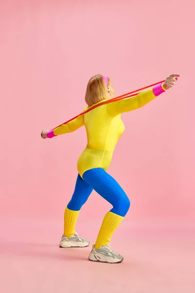 ピンクのスタジオを背景にフィットネス拡大とカラフルなスポーツウェアのトレーニングで高齢者のスポーツ女性のサイドビューイメージ スポーツライフスタイル 健康管理 健康の概念 — ストック写真