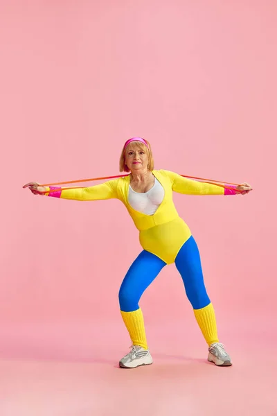 年长的女子在五颜六色的运动服训练中配备了健身器材 在粉红的工作室背景下摆姿势 运动生活方式 医疗保健 健康的概念 — 图库照片