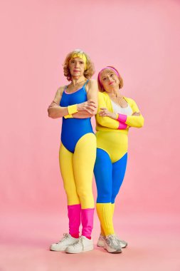 Renkli spor kıyafetleri içinde iki yaşlı kadın pembe stüdyo geçmişine karşı poz veriyor. Fitness. Formda kalıyorum. Sportif yaşam tarzı, emeklilik, sağlık, sağlık. Ad