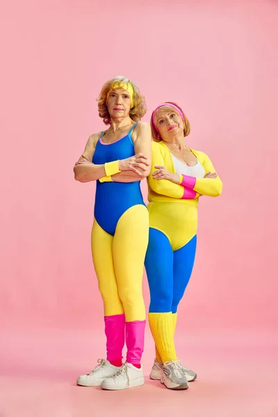 Dwie Starsze Kobiety Kolorowych Strojach Sportowych Pozujące Różowym Tle Studia — Zdjęcie stockowe