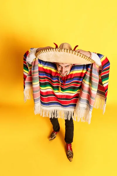カラフルなお祝いの服 ポンチョ 黄色のスタジオの背景に対してポーズいくつかのブレロで若い男のトップビューの肖像画 メキシコの伝統 楽しさ お祝い 感情の概念 — ストック写真