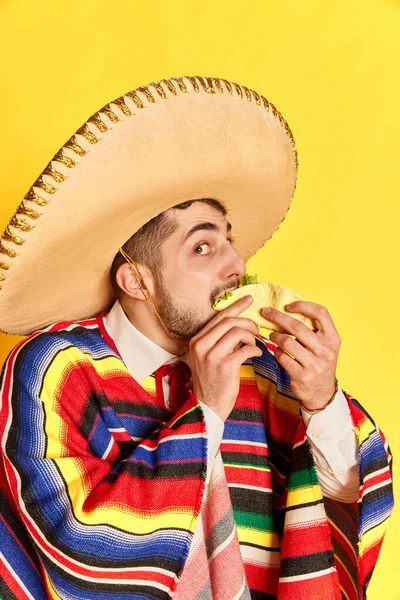 Portret Młodego Człowieka Kolorowych Świątecznych Ubraniach Ponczo Sombrero Jedzącego Taco — Zdjęcie stockowe