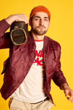 Stüdyonun arka planında müzik çalarıyla modern kıyafetleri zehirleyen duygusal genç adamın portresi. Duyguların kavramı, erkek modası, yaşam tarzı, yüz ifadesi. Ad