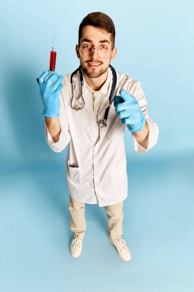 若いハンサムな男のトップビューの肖像画 青いスタジオの背景に対して注射器でポーズ白い医療ガウンの医師 注射だ 職業の概念 — ストック写真