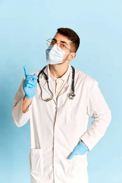医療警告だ 青のスタジオの背景に対してポーズを若い男 白い医療ガウン 保護マスクや手袋の医師の肖像画 職業の概念 — ストック写真