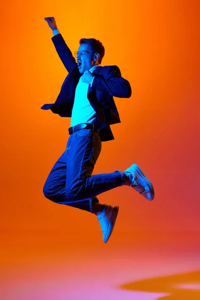 成功だ ネオンの光の中でオレンジのスタジオの背景に感情的にジャンプスタイリッシュな服の若い男の完全な長さの肖像画 ライフスタイルの概念 — ストック写真