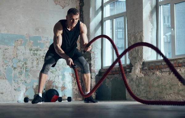 強さと耐久性 若い筋肉質の男は屋内で戦闘ロープのトレーニングを行う 機能訓練演習 スポーツライフスタイル ボディケア フィットネス 健康の概念 — ストック写真