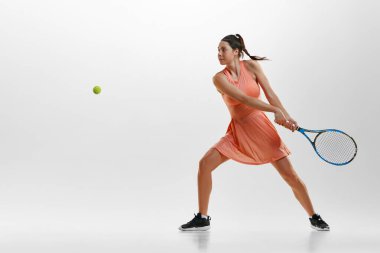 Rekabetçi genç bir kadının portresi, rahat spor kıyafetleri içinde tenis oynuyor, beyaz stüdyo geçmişine karşı antrenman yapıyor. Profesyonel spor, hareket, sağlık, eylem kavramı. Ad