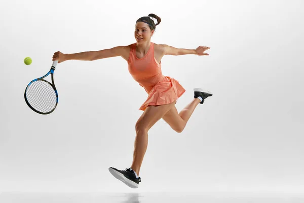 スポーツの制服を着た笑顔の若い女性の肖像画 トレーニング 白いスタジオの背景に対してテニスをプレイ ラケットでボールを打つ プロスポーツ 行動の概念 — ストック写真