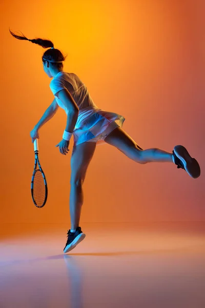 ネオンライトのオレンジスタジオの背景を背景にした均一な訓練での女性テニス選手の全長バックビューイメージ ゲームだ プロスポーツ 行動の概念 — ストック写真