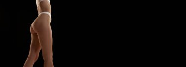 İnce kadın bacakları ve kalçalarının kırpılmış görüntüsü. Siyah stüdyo geçmişine karşı iç çamaşırlarıyla poz veren kadın model. Vücut ve cilt bakımı kavramı, şekil, zindelik, sağlık. Reklam için boşluk kopyala. Pankart