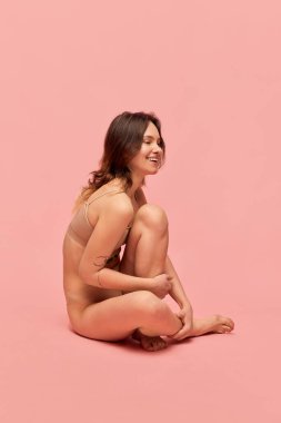 Şefkatli, pozitif, bej iç çamaşırlı genç bir kızın portresi pembe stüdyo arka planında poz veriyor. Zayıf, sağlıklı bir vücut. Vücut ve cilt bakımı kavramı, figür, form, sağlık, sağlık.