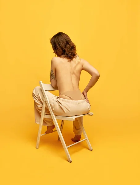 ジーンズ姿の椅子に腰を下ろし 黄色のスタジオを背景にポーズをとる少女のリアビュー 美しさ 身体とスキンケア フィギュア フィットネス ウェルネスの概念 — ストック写真