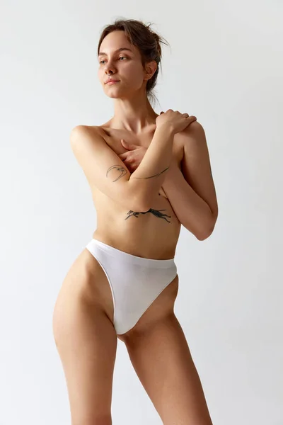 Portret Młodej Szczupłej Dziewczyny Tatuażami Zakrywającej Piersi Rękami Pozującej Bieliźnie — Zdjęcie stockowe