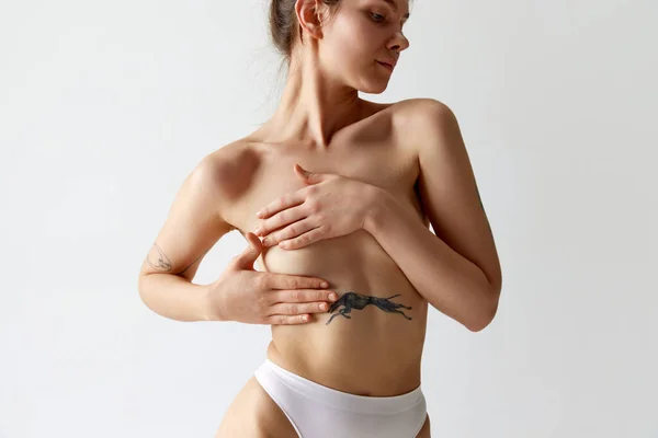 剪下的苗条身材的小女孩用手捂住乳房 在灰色的工作室背景下摆出内裤的形象 女性保健 身体和皮肤护理 整形手术 健康的概念 — 图库照片