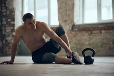 Sıkı bir antrenmandan sonra yorgun hissediyorum. Genç kaslı adam terli vücutla yerde üstsüz oturuyor. Spor yaşam tarzı, vücut bakımı, fitness, hobi, sağlık, eylem ve hareket kavramı