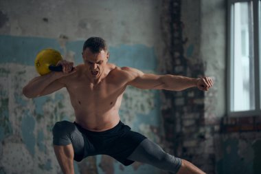Güç ve dayanıklılık. Güçlü kaslı, rahatlamış, üstsüz vücut eğitimi almış, gündüz vakti ağırlık kaldıran genç bir adam. Spor yaşam tarzı, vücut bakımı, fitness, hobi, sağlık