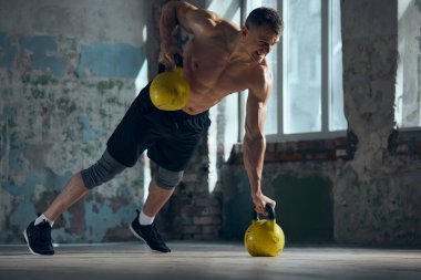 Kaslı, güçlü, formda, spor malzemeleriyle gündüz vakti evde antrenman yapan yakışıklı bir genç. Ağırlık kaldırıyorum. Spor yaşam tarzı, vücut bakımı, fitness, hobi, sağlık