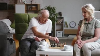Mutlu yaşlı çift, emekli erkek ve kadın evde birlikte satranç oynayıp çay içerek vakit geçiriyorlar. Boş zaman ve hobi. Aile kavramı, ilişki, emeklilik, yaşam tarzı, mutluluk