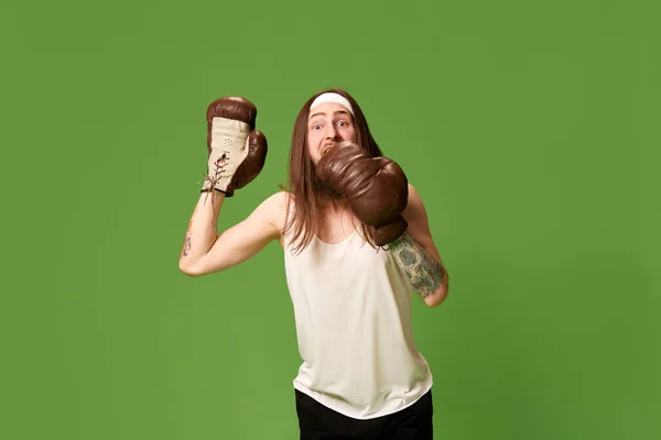 感情用事的体育竞赛 年轻男子的画像 棕色长发 头戴单色皮制拳击手套 背景为绿色工作室 面部表情的概念 — 图库照片