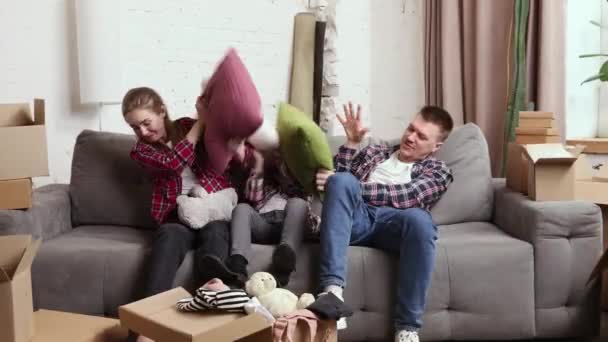 快乐快乐的年轻家庭 父母坐在沙发上 和小女儿一起玩枕头 搬进新公寓 房地产 新生活的概念 — 图库视频影像