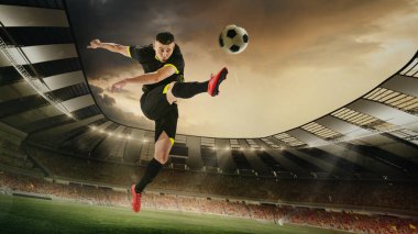 Genç bir adam, profesyonel bir futbolcu. Akşamları üç boyutlu stadyumda topa vuruyor. Arka planda bulanık seyirci var. Maç, spor, rekabet, aksiyon ve hareket, oyun, kupa kavramı.