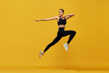 Spor giyim eğitimindeki genç ve güzel bir kızın dinamik görüntüsü sarı stüdyo arka planında koşuyor. Kardiyo seansı. Spor anlayışı, sağlıklı ve aktif yaşam tarzı, güzellik, fitness