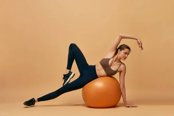 保持身体苗条 灵活的女孩在橙色工作室的背景下做伸展运动 带着健身球 健康和积极的生活方式 健康的概念 — 图库照片
