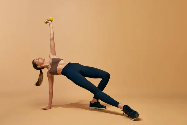 体重機器でスポーツボディトレーニングと美しい若い女の子 オレンジのスタジオの背景に対するダンベル ストレッチ練習 スポーツ 健康的でアクティブなライフスタイル 美しさ フィットネスコンセプト — ストック写真
